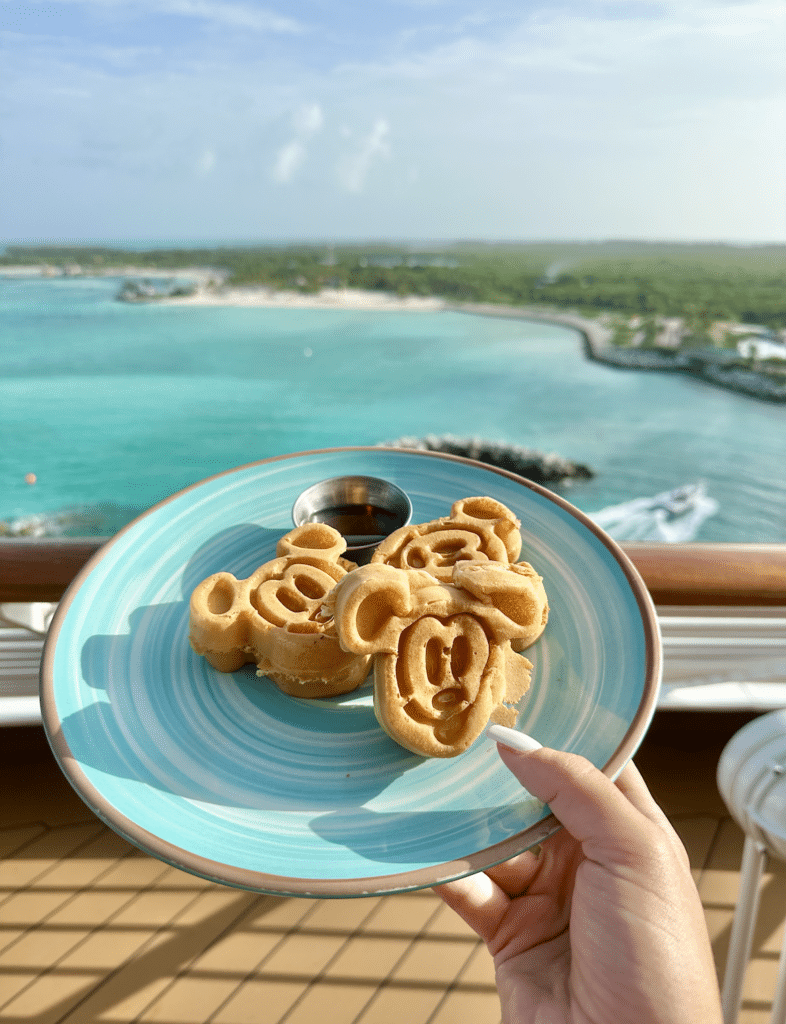 Plate of Mickey Mouse waffles with syrup, overlooking turquoise waters on a Disney Cruise.